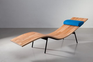 Moderne Relaxliege aus geformtem Holz mit schwarzem Gestell und blauem Kopfpolster in Galerieumgebung.