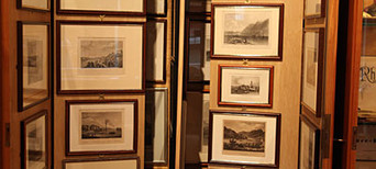 Schrank mit zahlreichen gerahmten Zeichnungen und Stichen historischer Bauwerke und Landschaften.