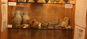 Beleuchtete Museumsvitrine mit historischen Keramikgefäßen, Scherben und Ausgrabungsplänen.