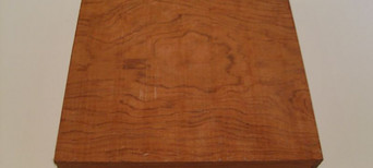 Massiver, quadratischer Holzblock mit rötlich-brauner Oberfläche und leichter Struktur.