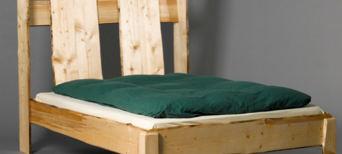 Massives Bett aus naturbelassenem Holz mit unregelmäßig geformtem Kopfteil und grüner Bettdecke.