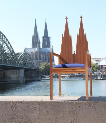 Holzstuhl mit Rückenlehne in Form der Kölner Domspitzen, aufgestellt vor dem Rhein mit Blick auf den Kölner Dom