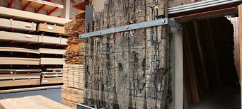 Erhaltene Holzpfähle einer römischen Rheinbrücke, ausgestellt neben gestapelten Holzplatten im Lager.