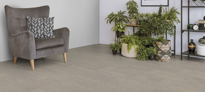 Der Boden im Wohnzimmer ist mit hellgrauem Kork belegt. Es gibt einen bequemen Sessel und einen Ständer mit Grünpflanzen.
