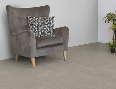 Der Boden im Wohnzimmer ist mit hellgrauem Kork belegt. Es gibt einen bequemen Sessel und einen Ständer mit Grünpflanzen.