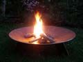 Brennende Feuerschale aus Metall mit Holzscheiten im Garten bei Dämmerung.